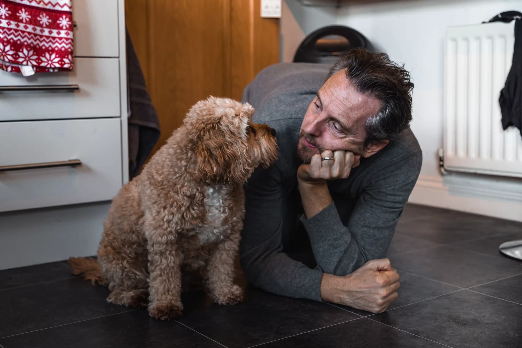 Un homme allongé sur le sol de sa cuisine, face à son chien qui le regarde
